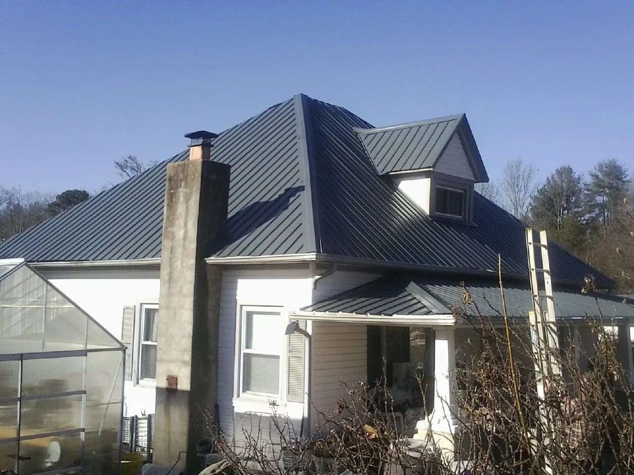 Dark blue standing seam metal roof on a white farmhouse with dormer — Slate & Tile Roof Repair by Roofing Brothers in Milliken