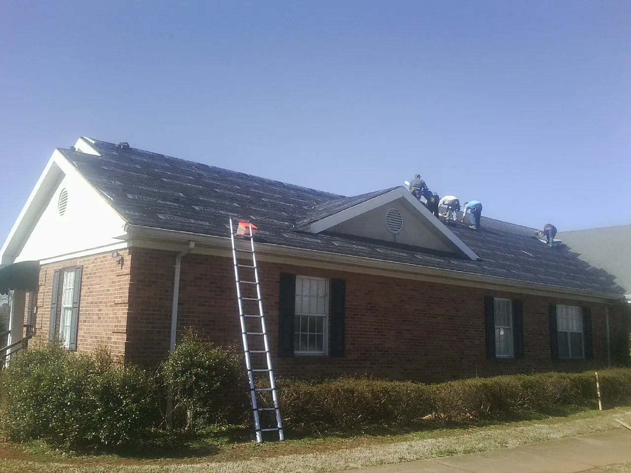 Crew tearing shingles off a brick ranch roof with a ladder set — Emergency Roof Repair work by our crew in Milliken