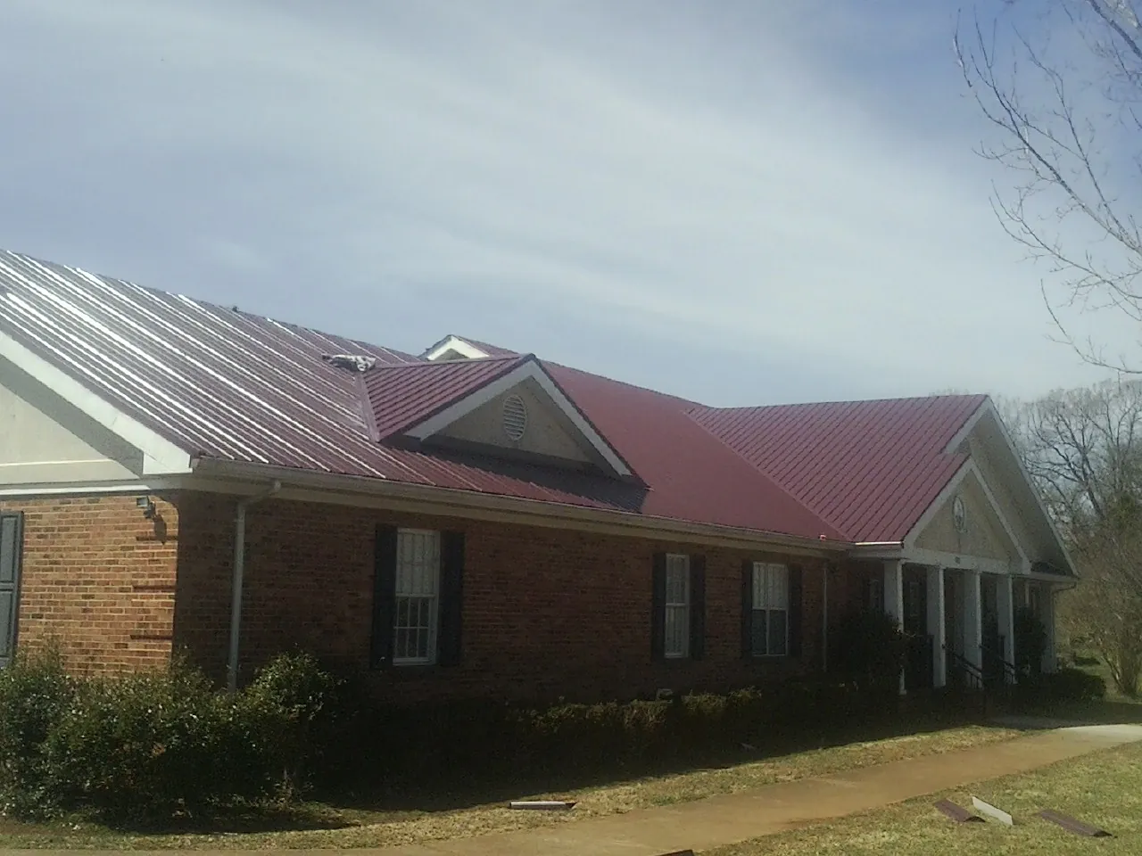 Red metal roof with gabled entries on a long brick building, from a Hail Damage Roof Repair job in Milliken