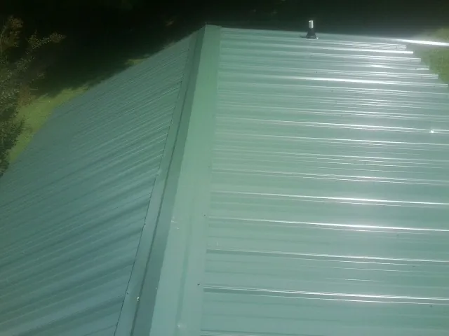 New green metal panels meeting at the ridge of a roof — Flat Roof Repair work by our crew in Milliken