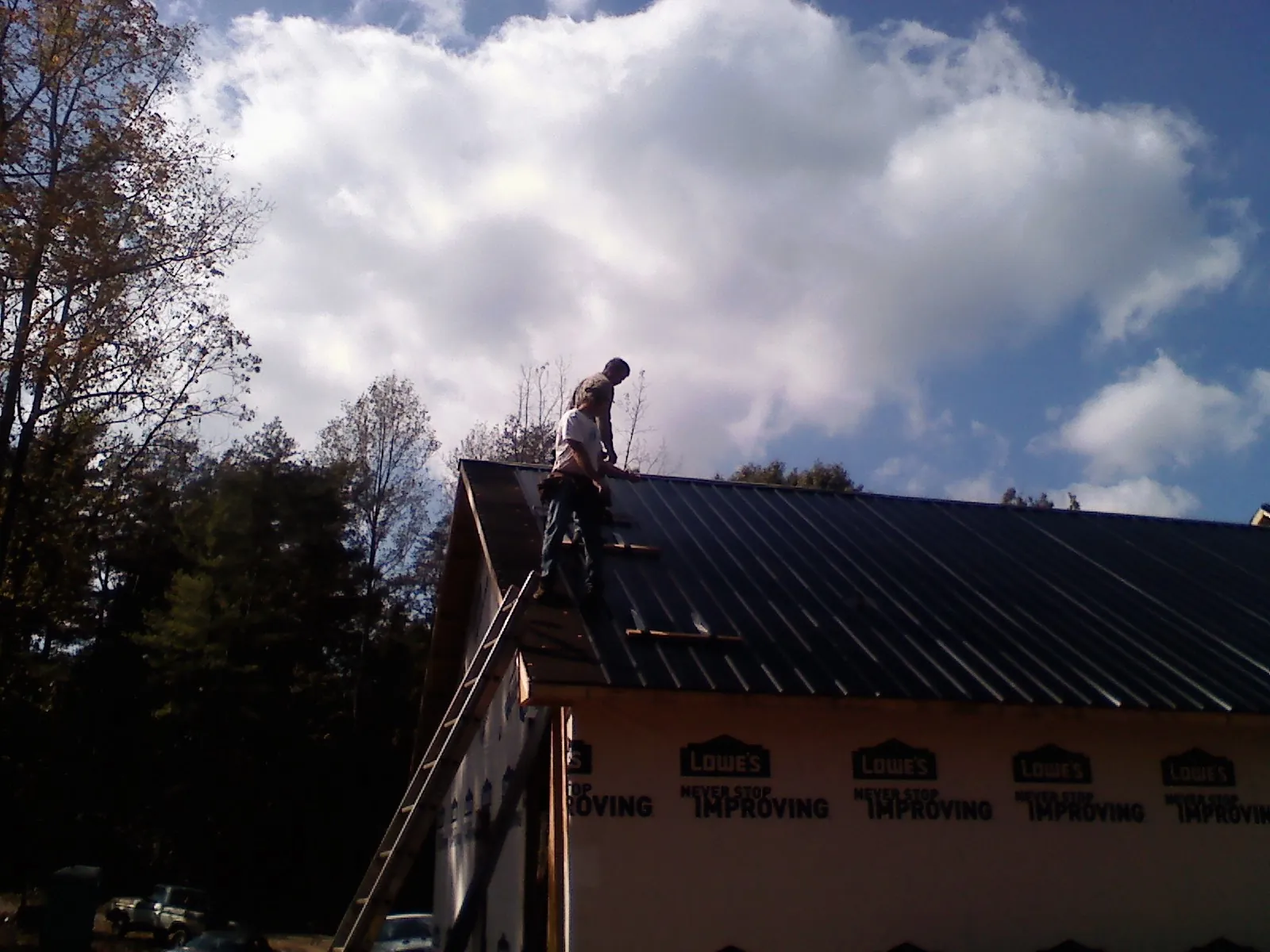 Roofer fastening dark metal panels high against a cloudy sky, from a Roof Inspection job in Milliken