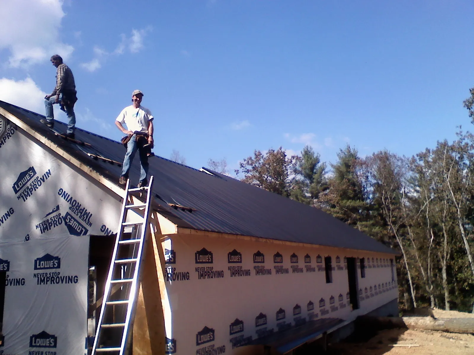 Two roofers standing on a long dark metal roof over a wrapped building in Milliken