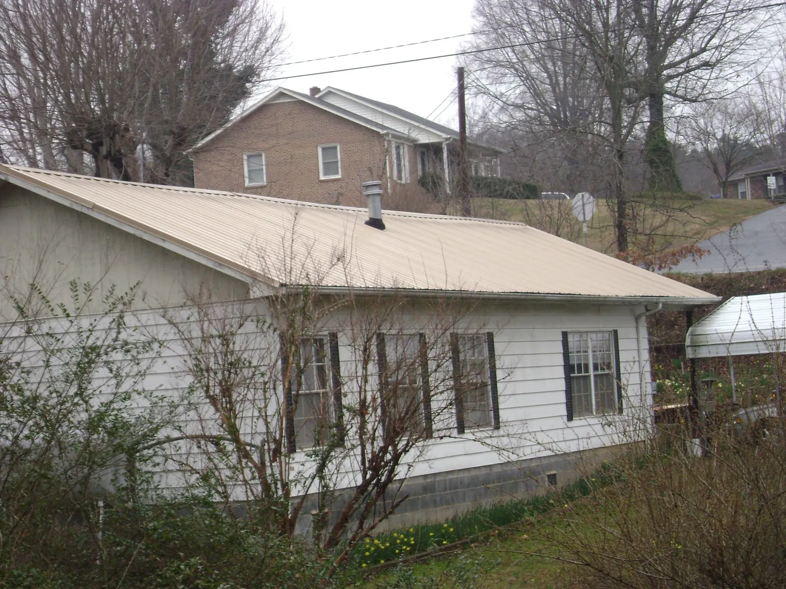 Tan metal roof on a white sided house set into a hillside — Commercial Roofing by Roofing Brothers in Milliken